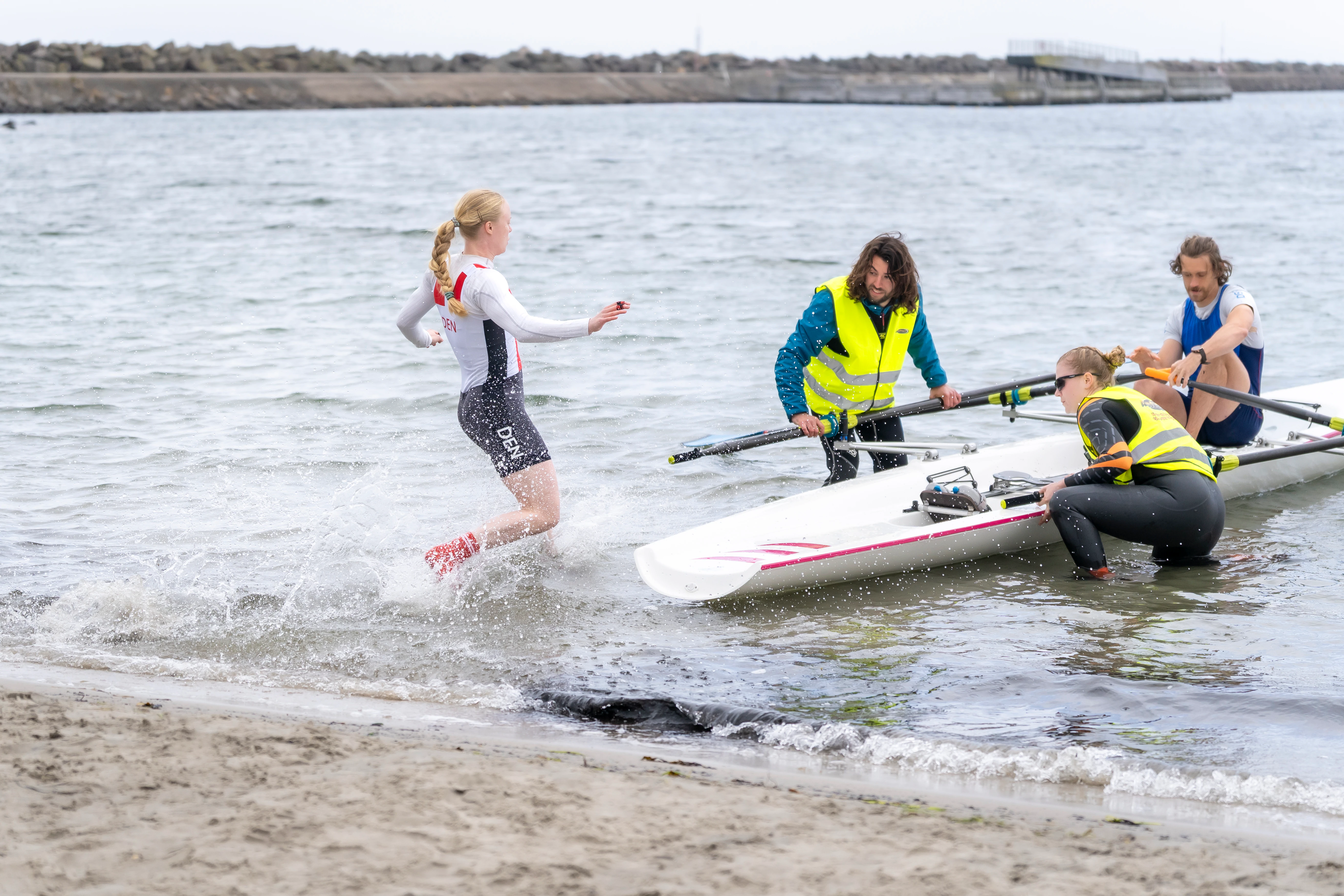AI-mockup af Beach Sprint-atleter i eksplosiv funktionel træning med slæde, kettlebells og korte ergometerintervaller.