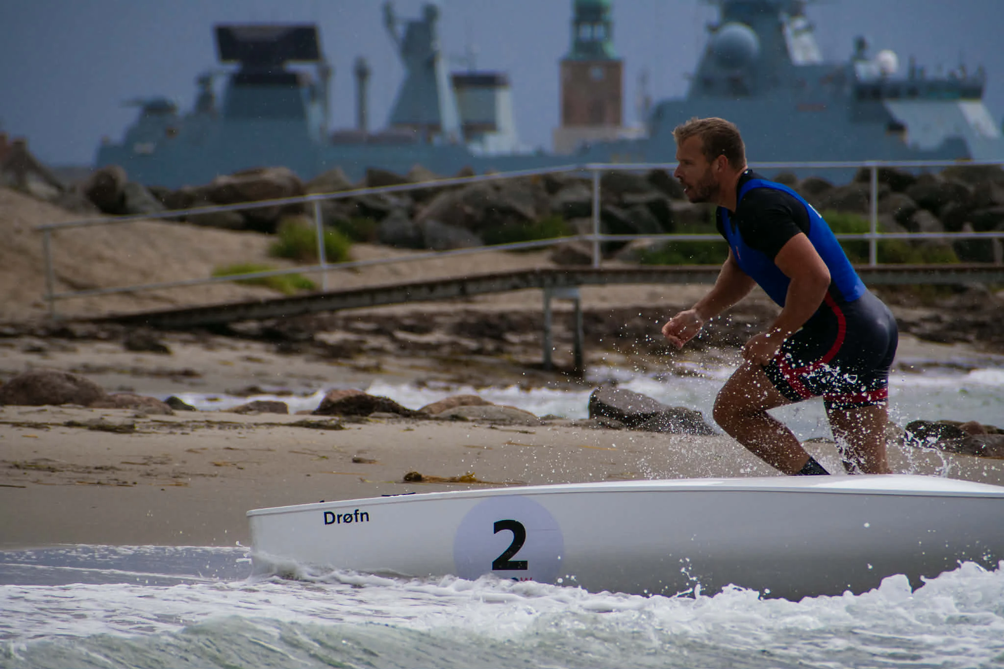 AI-mockup af Beach Sprint-atleter, der spurter gennem sandet med en coastalbåd mod bølgerne.